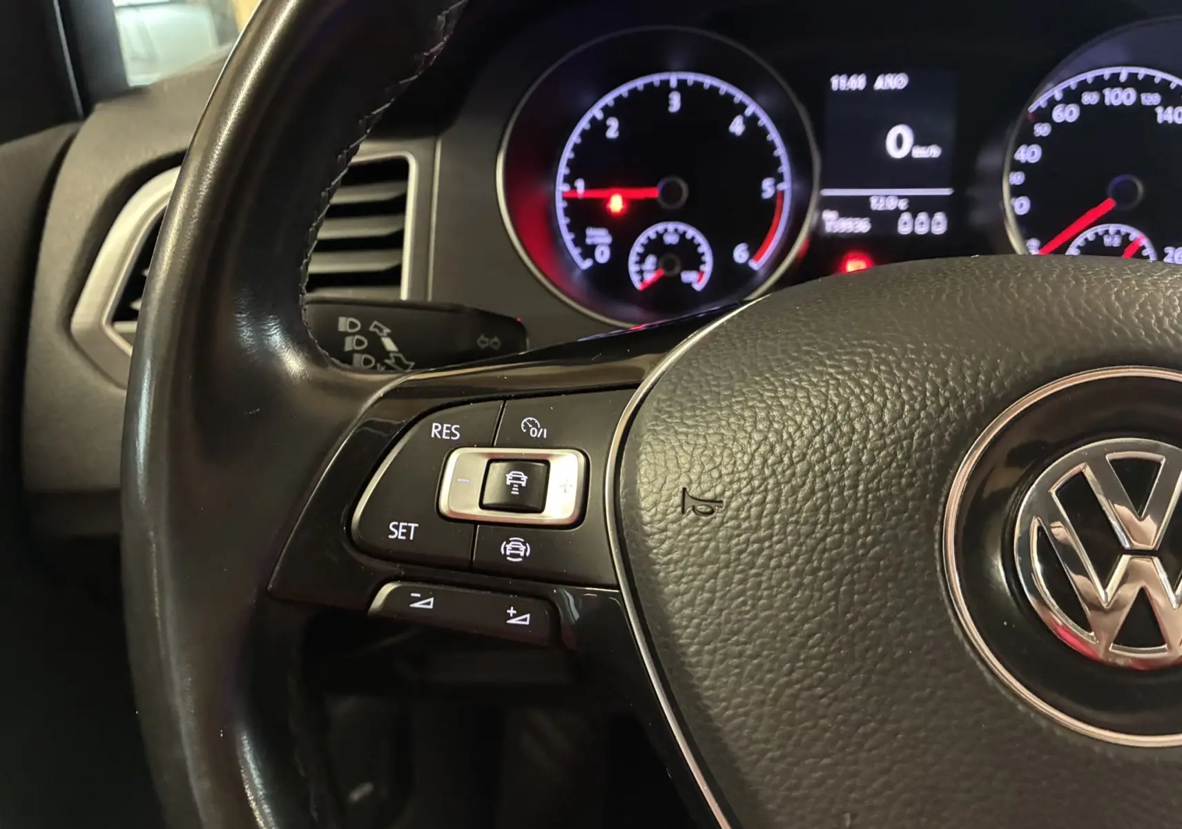 Gros plan sur le volant noir de la Volkswagen Golf Sportsvan 2019 avec commandes de régulateur et tableau de bord éclairé.