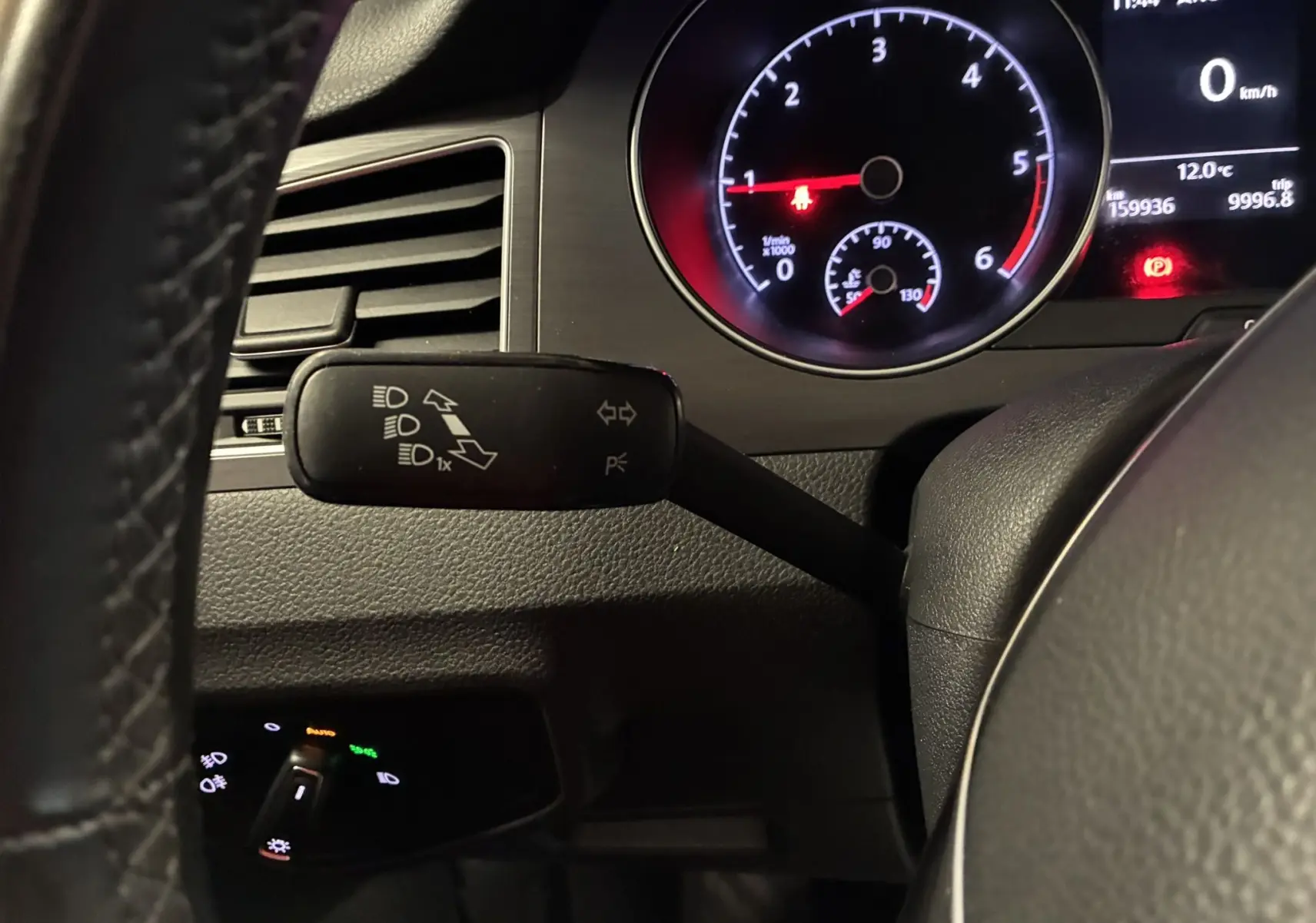 Gros plan sur le commodo gauche et le tableau de bord éclairé d'une Volkswagen Golf Sportsvan gris, intérieur sombre.