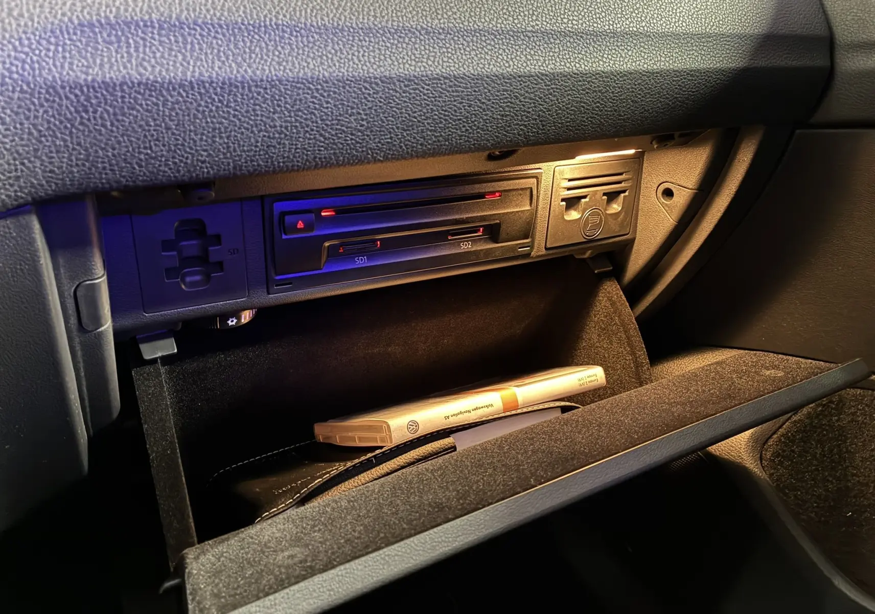 Gros plan sur la boîte à gants ouverte du Volkswagen Golf Sportsvan gris, montrant lecteur SD et manuel dans l'habitacle.