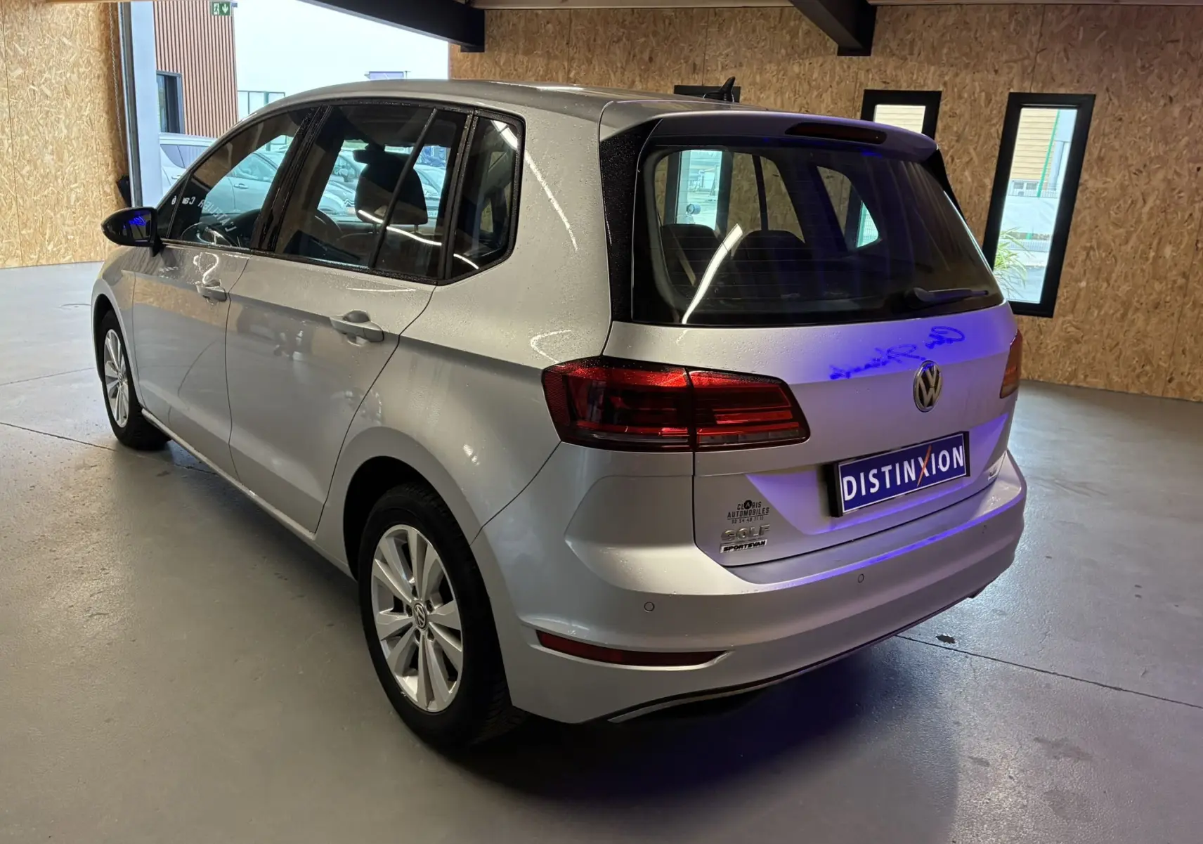 Vue 3/4 arrière droit d'une Volkswagen Golf Sportsvan gris métallisé dans un garage lumineux.