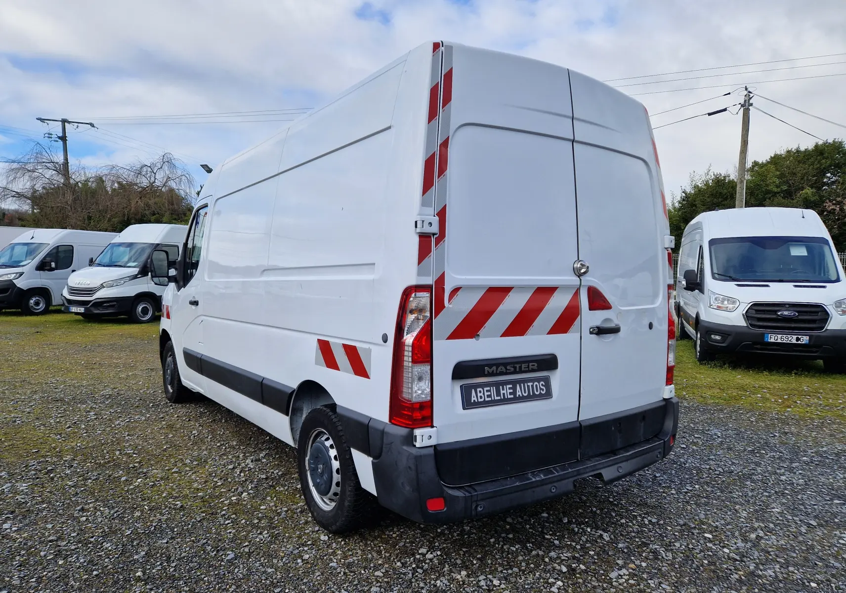 Vue 3/4 arrière droite d’un Renault Master blanc avec bandes réfléchissantes rouges et noires sur pare-chocs et flanc.