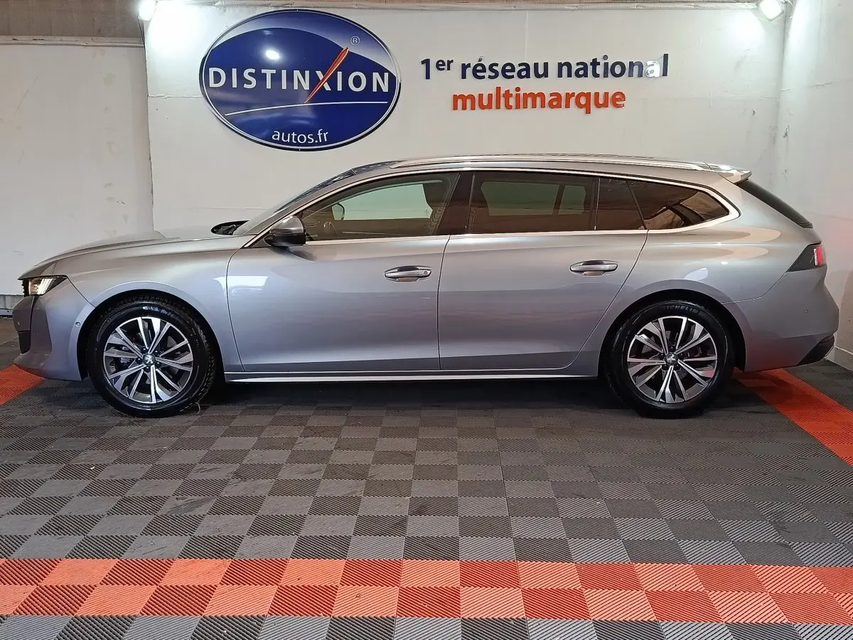Profil droit d'une Peugeot 508 break gris clair 2020, avec jantes alliage et vitres teintées, en intérieur showroom.