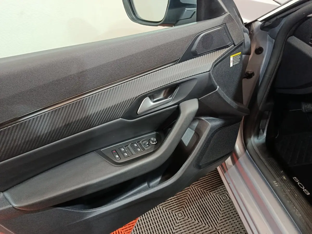 Vue rapprochée de la porte avant gauche gris clair du Peugeot 508 avec commandes électriques et habillage carbone.
