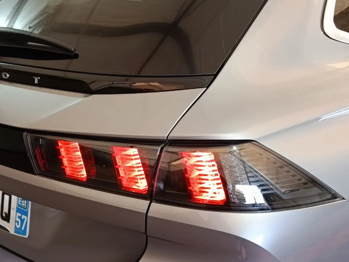 Feu arrière droit allumé sur Peugeot 508 gris clair, vue rapprochée du coin arrière du véhicule.