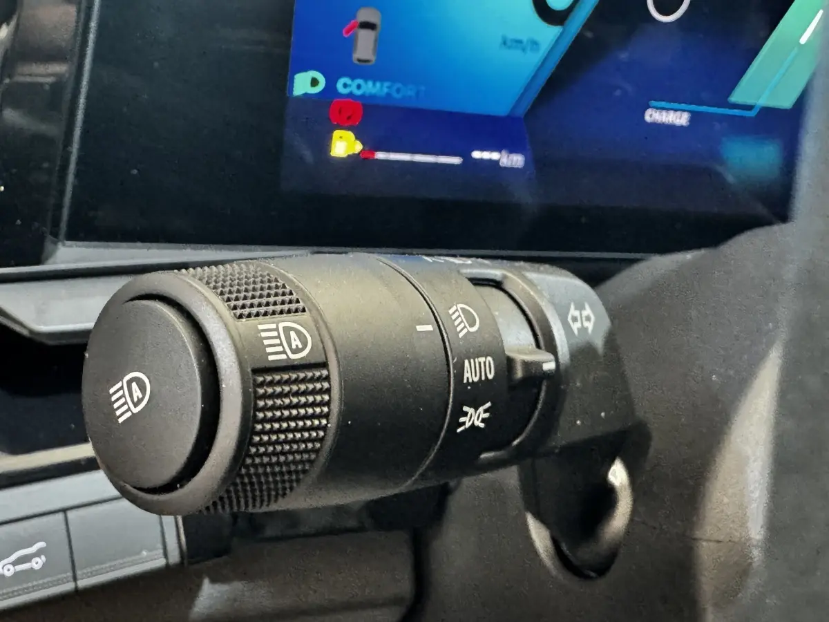 Gros plan sur la commande des phares automatique du Renault Espace noir 2025, avec écran multifonctions en arrière-plan.
