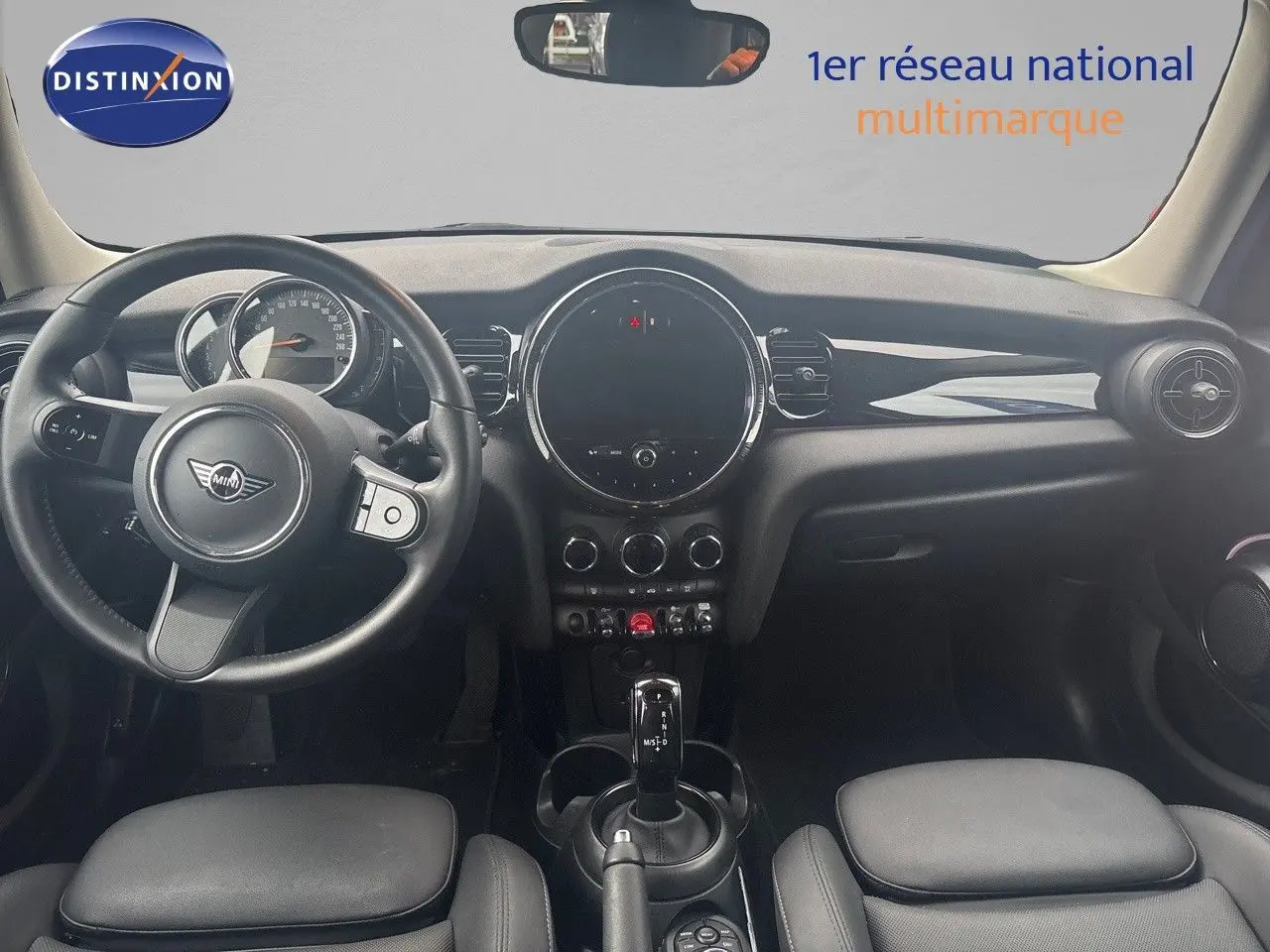 Intérieur avant d'une MINI 1.5 136CH gris, tableau de bord noir avec volant et console centrale visibles.