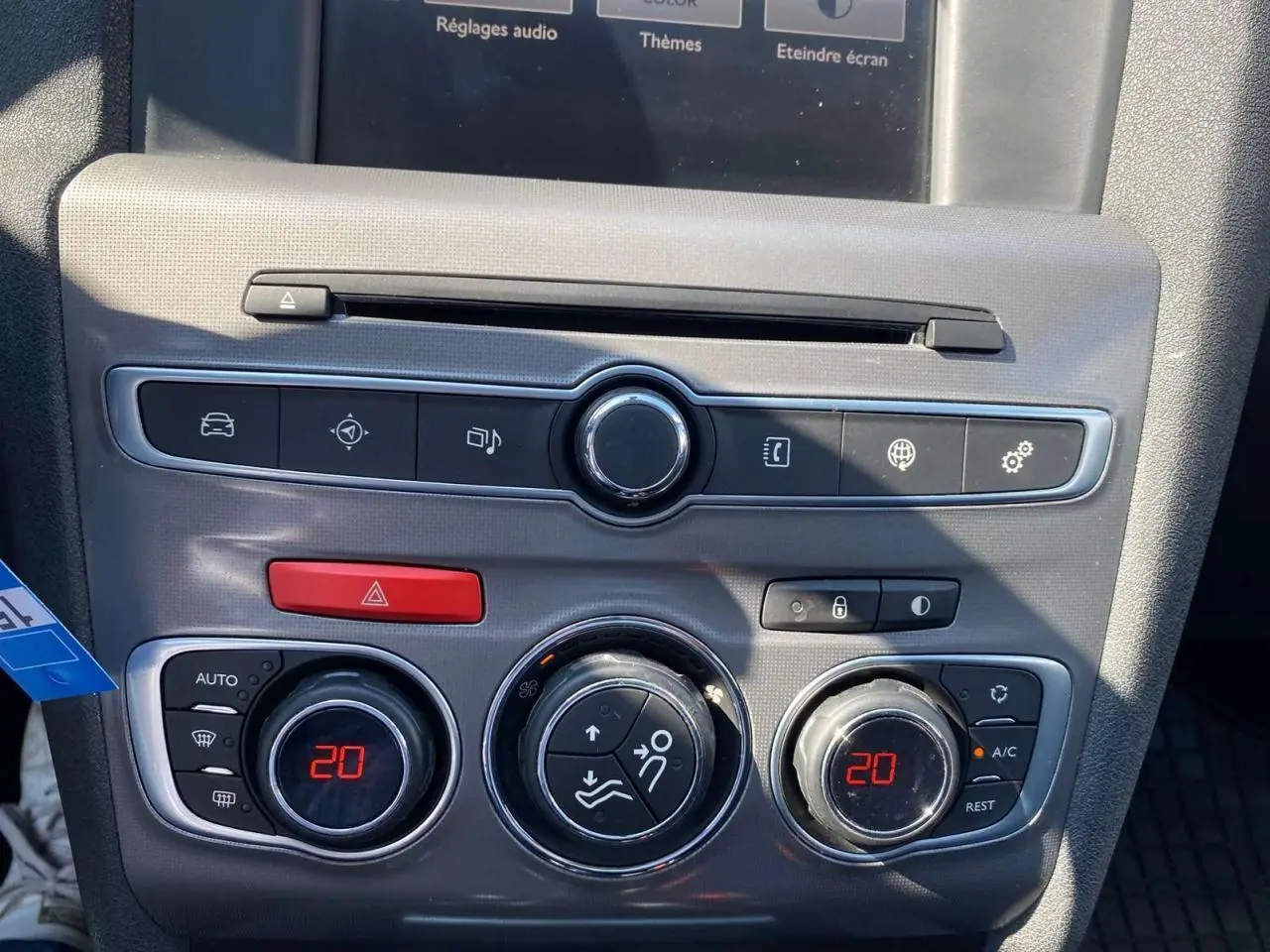 Vue rapprochée de la console centrale grise d'une Citroën C4 rouge 2015, avec commandes climatisation à 20°C.
