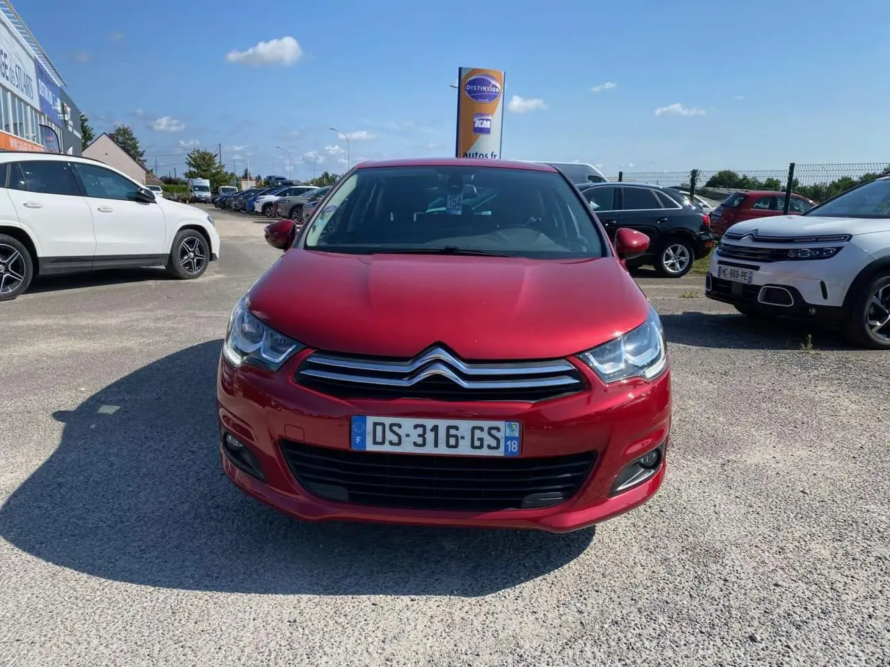 Vue de face d'une Citroën C4 rouge métallisée 2015 avec projecteurs antibrouillard sur un parking extérieur.