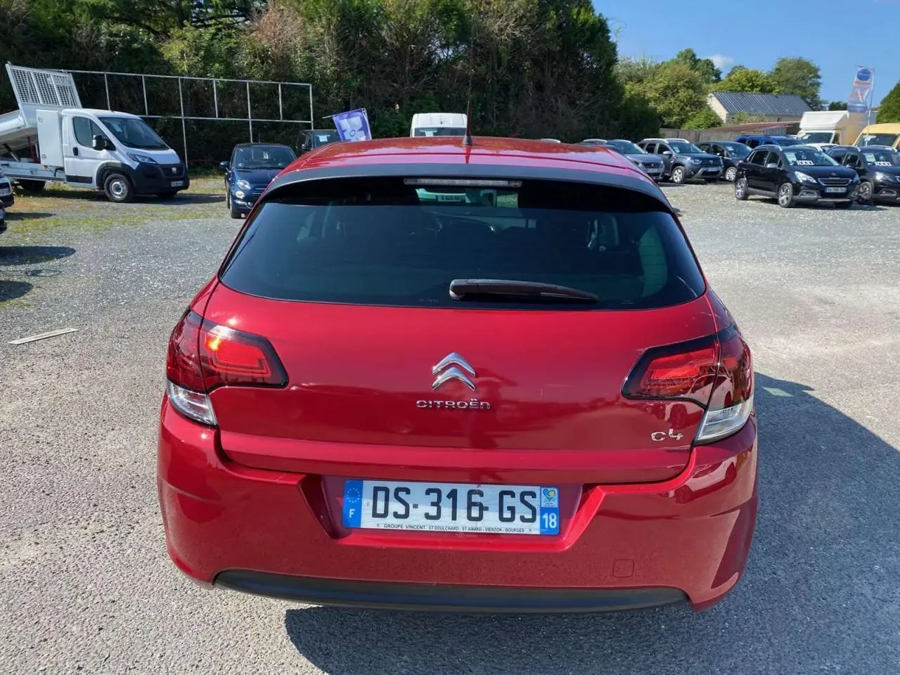 Vue arrière d'une Citroën C4 rouge métallisée de 2015 avec plaques françaises, stationnée sur un parking extérieur.