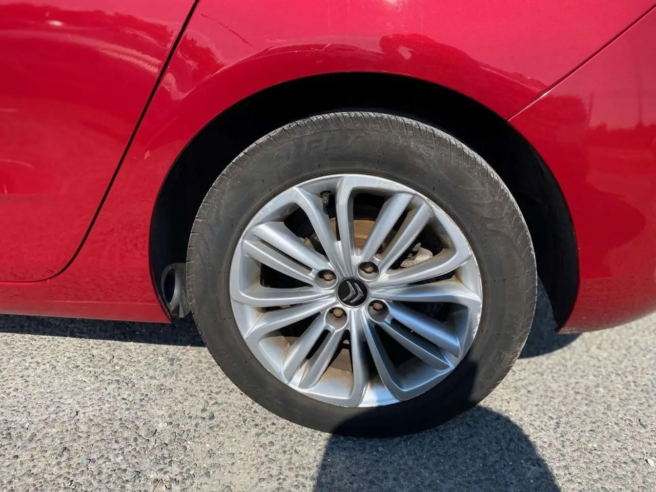 Gros plan sur la roue arrière gauche d'une Citroën C4 rouge métallisée de 2015 avec jante alliage distinctive.