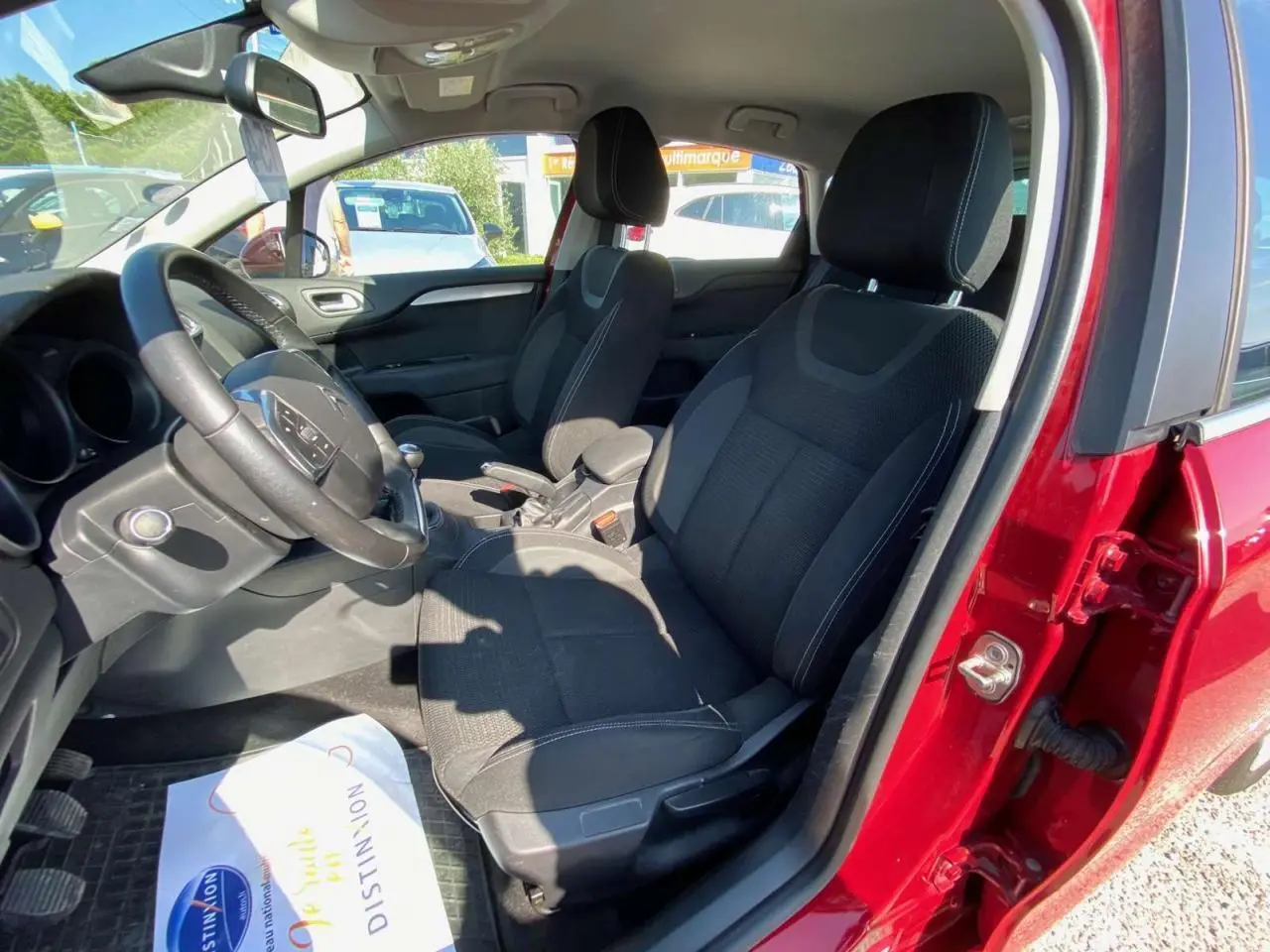 Vue intérieure côté conducteur d'une Citroën C4 rouge 2015, sièges noirs et volant avec commandes intégrées.