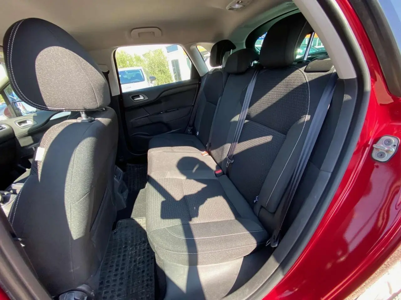 Vue intérieure de la banquette arrière noire d'une Citroën C4 rouge 2015, porte arrière droite ouverte.