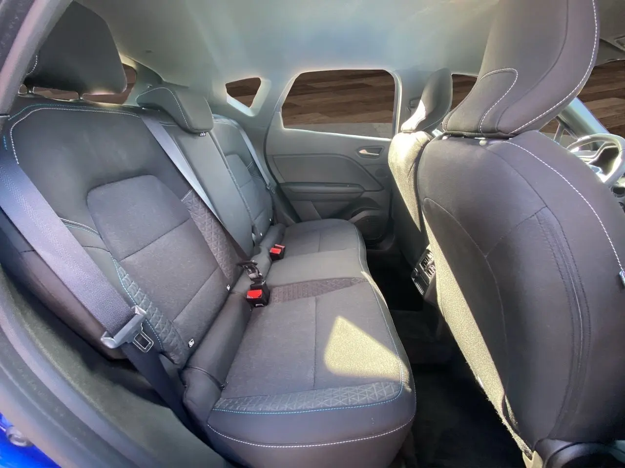 Vue intérieure arrière du Renault Captur 2024, sièges tissu noir avec surpiqûres bleues et ceintures de sécurité visibles.