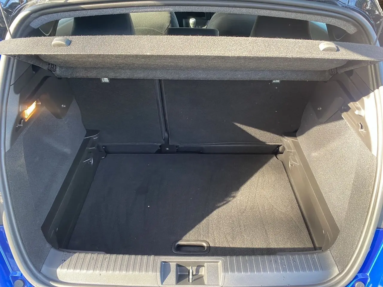 Coffre ouvert du Renault Captur TCE 90 Evolution 2024 bleu iron avec toit noir, vue arrière montrant l'espace de chargement vide.