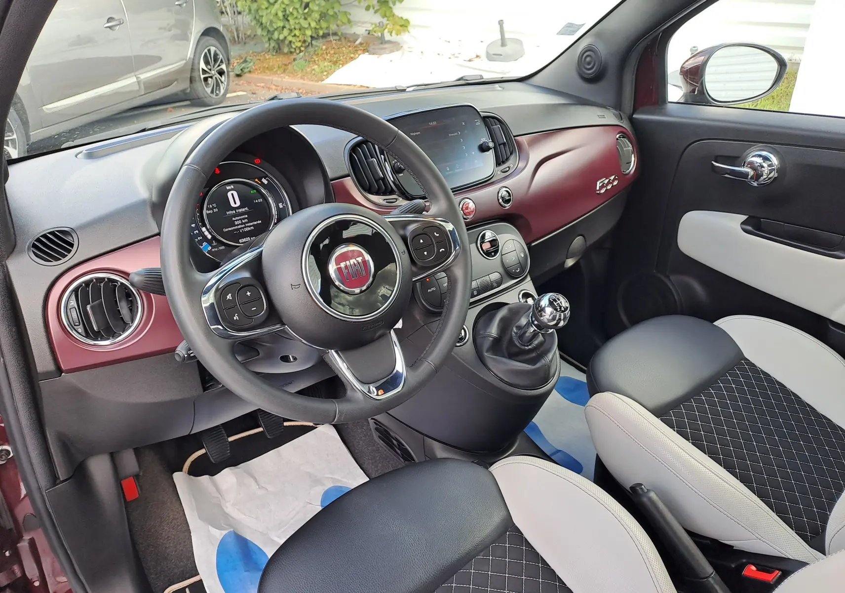 Vue intérieure côté conducteur de la Fiat 500 2020 avec tableau de bord bordeaux Opera et sièges bi-color noir et beige.