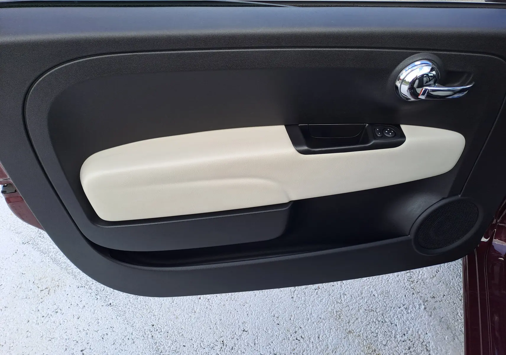 Gros plan sur la porte côté gauche de la FIAT 500 Opera Bordeaux Metal, avec garniture beige et poignée chromée.