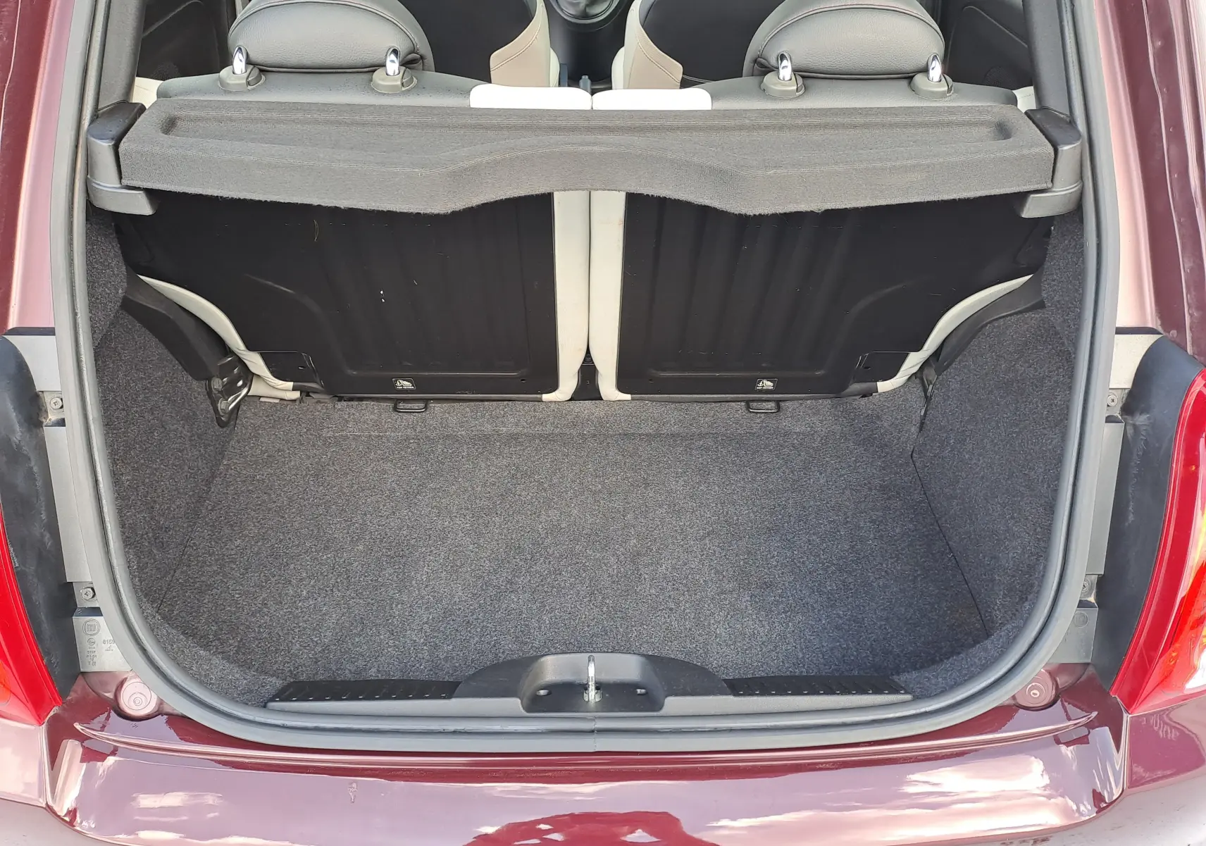 Coffre ouvert vu de l'arrière d'une FIAT 500 Opera Bordeaux Metal, montrant l'espace de chargement et les dossiers de sièges noirs.