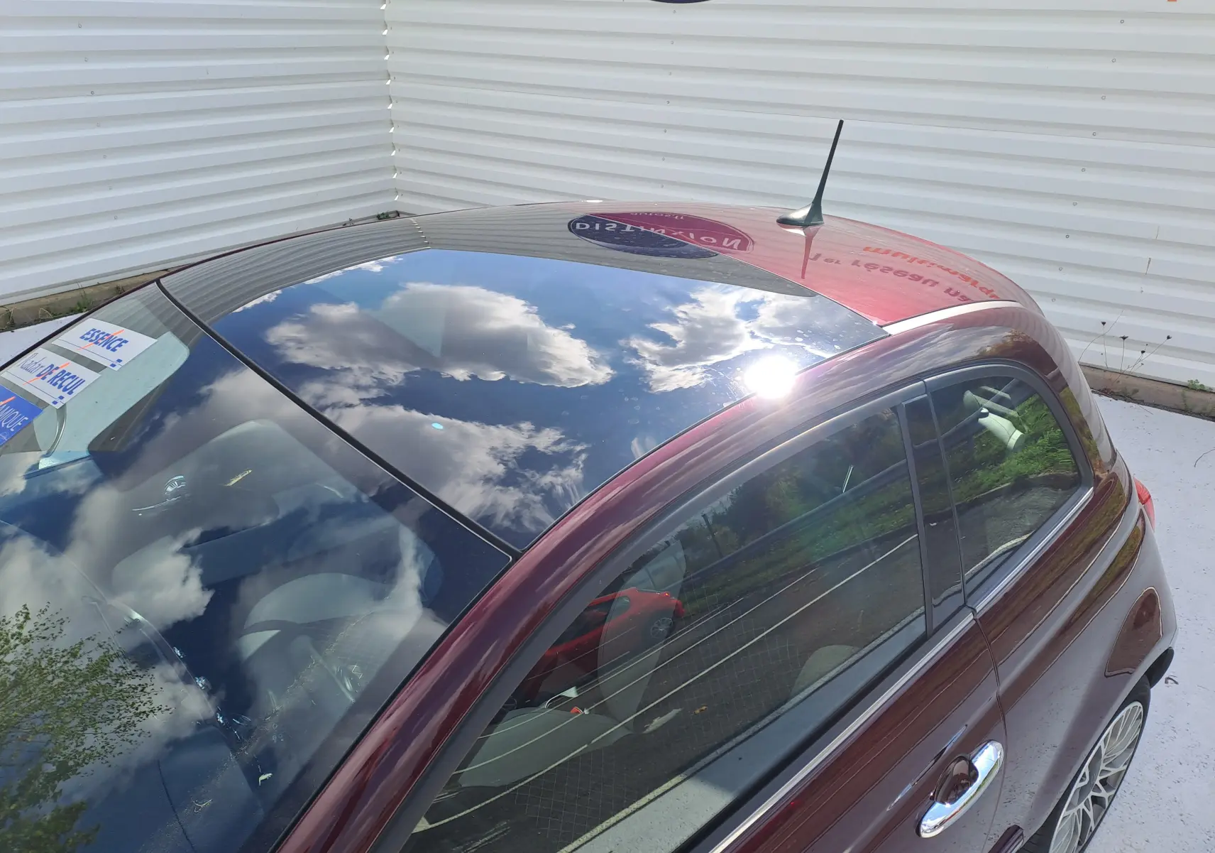 Vue plongeante sur le côté gauche d'une Fiat 500 Opera Bordeaux Métal 2020 avec toit vitré brillant et intérieur clair.