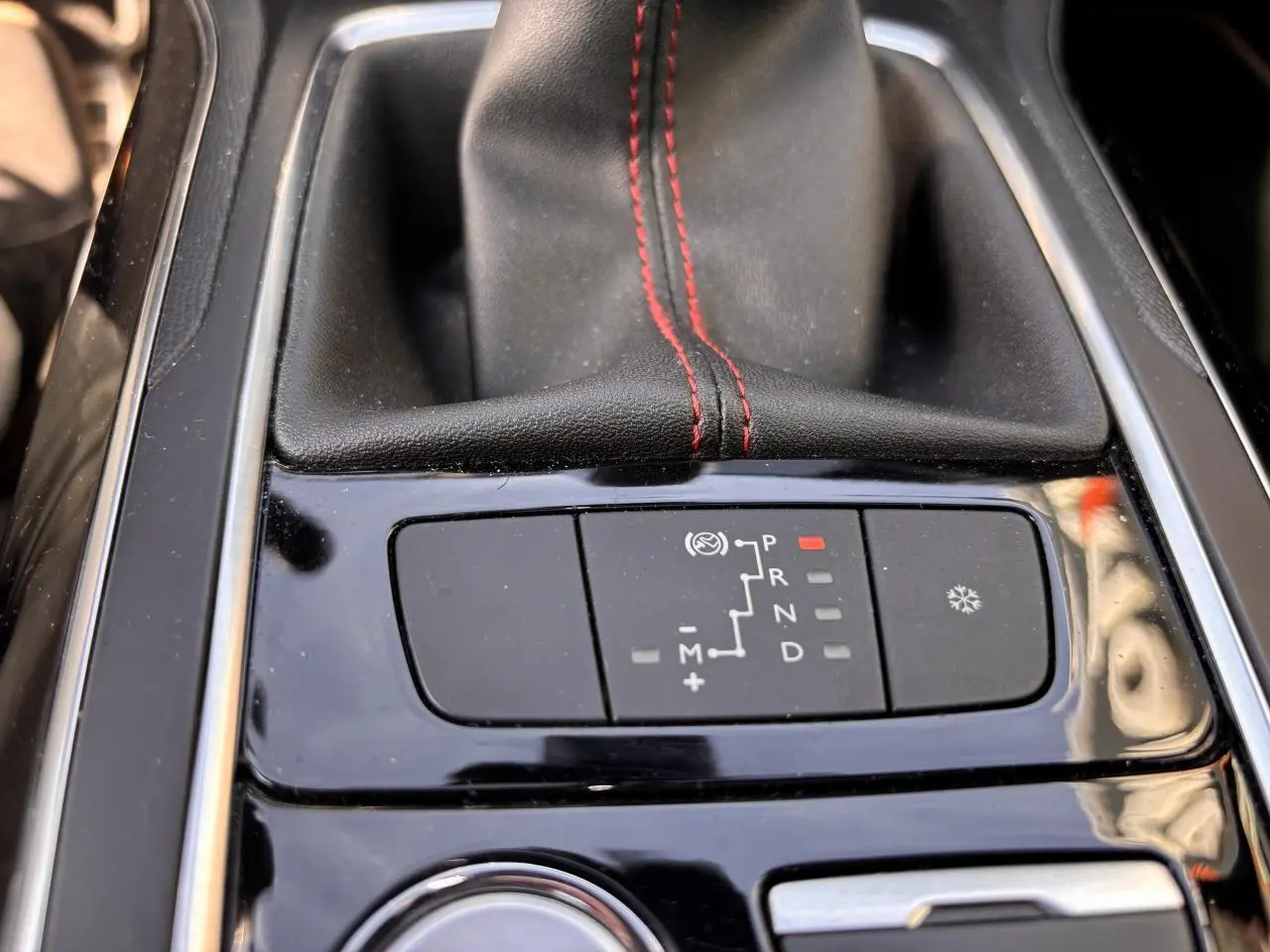 Gros plan sur la console centrale noire brillante de la Peugeot 308 GT Line avec levier de vitesse cuir noir et surpiqûres rouges.
