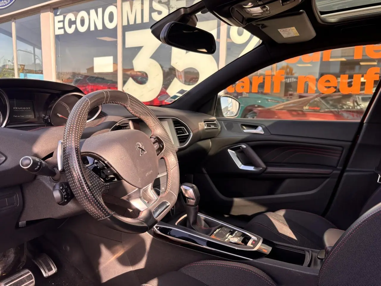 Intérieur avant droit de la Peugeot 308 GT Line 2016 avec volant cuir perforé et surpiqûres rouges visibles.