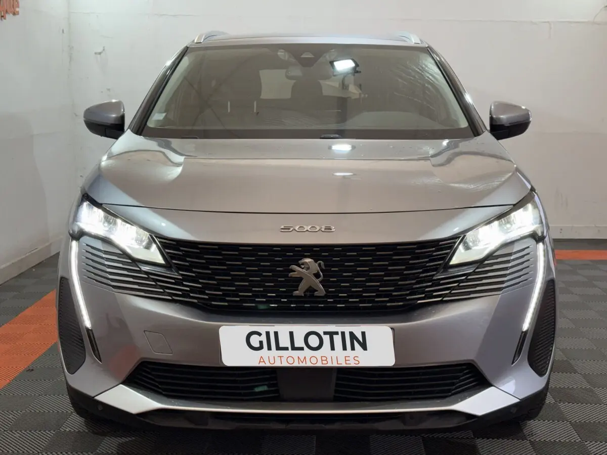 Vue frontale d’un Peugeot 5008 gris clair avec phares LED allumés et calandre noire distinctive.