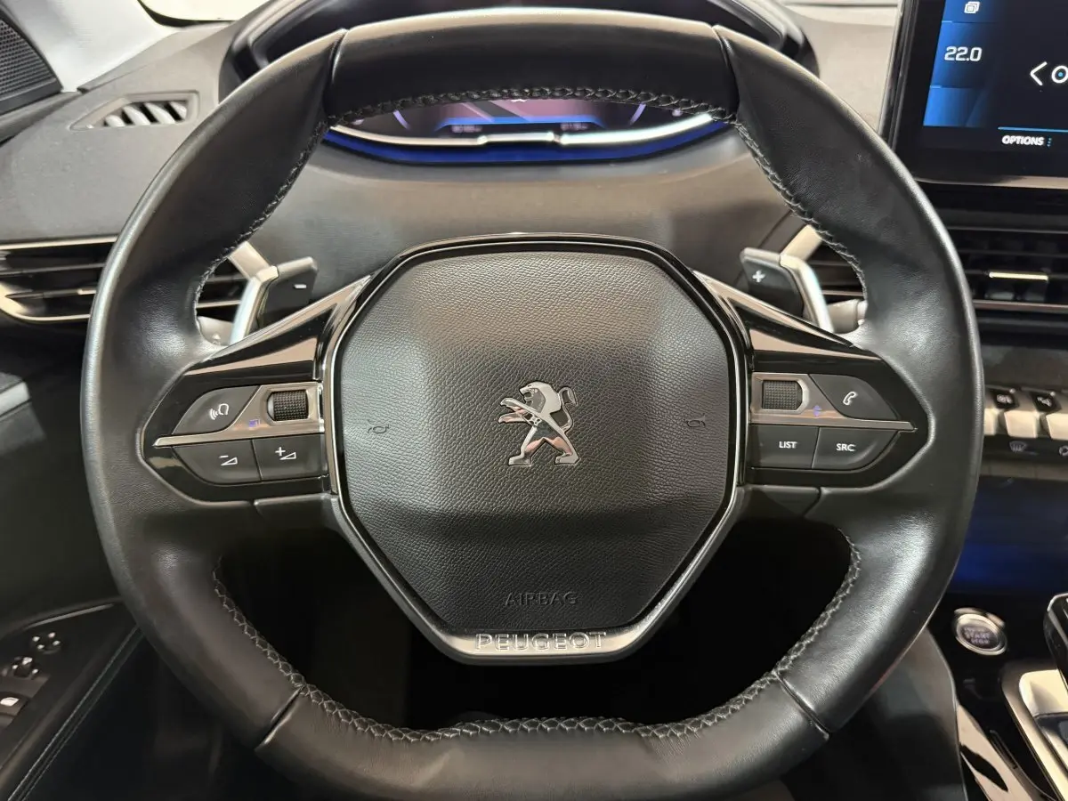 Volant cuir noir de Peugeot 5008 2021 avec commandes intégrées et logo lion au centre, vue de face rapprochée.