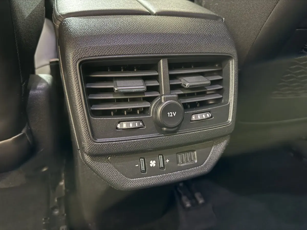 Gros plan sur la console arrière noire du Peugeot 5008 2021 avec ventilation, prise 12V et commandes climatisation.