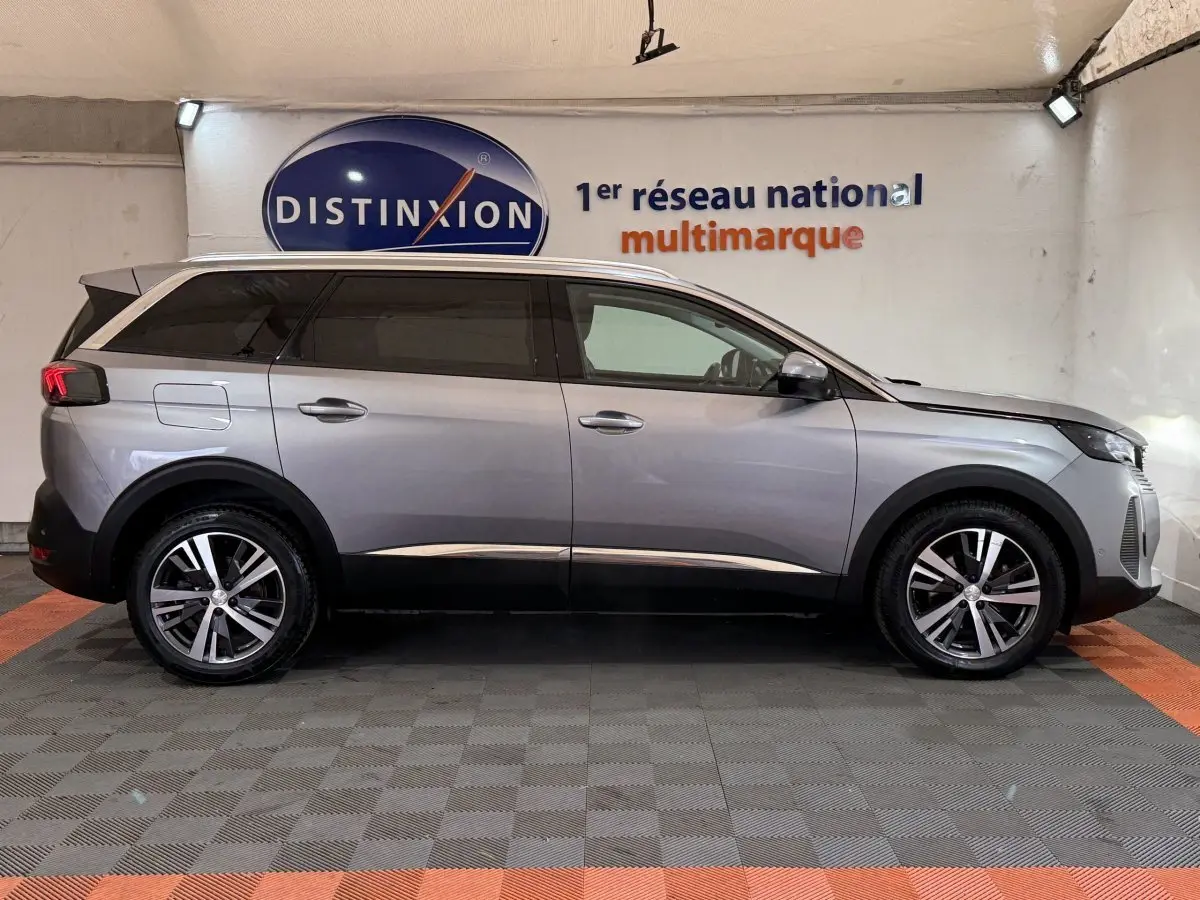 Profil droit d'un Peugeot 5008 gris clair 2021, SUV familial avec jantes alliage et vitres teintées, en intérieur showroom.