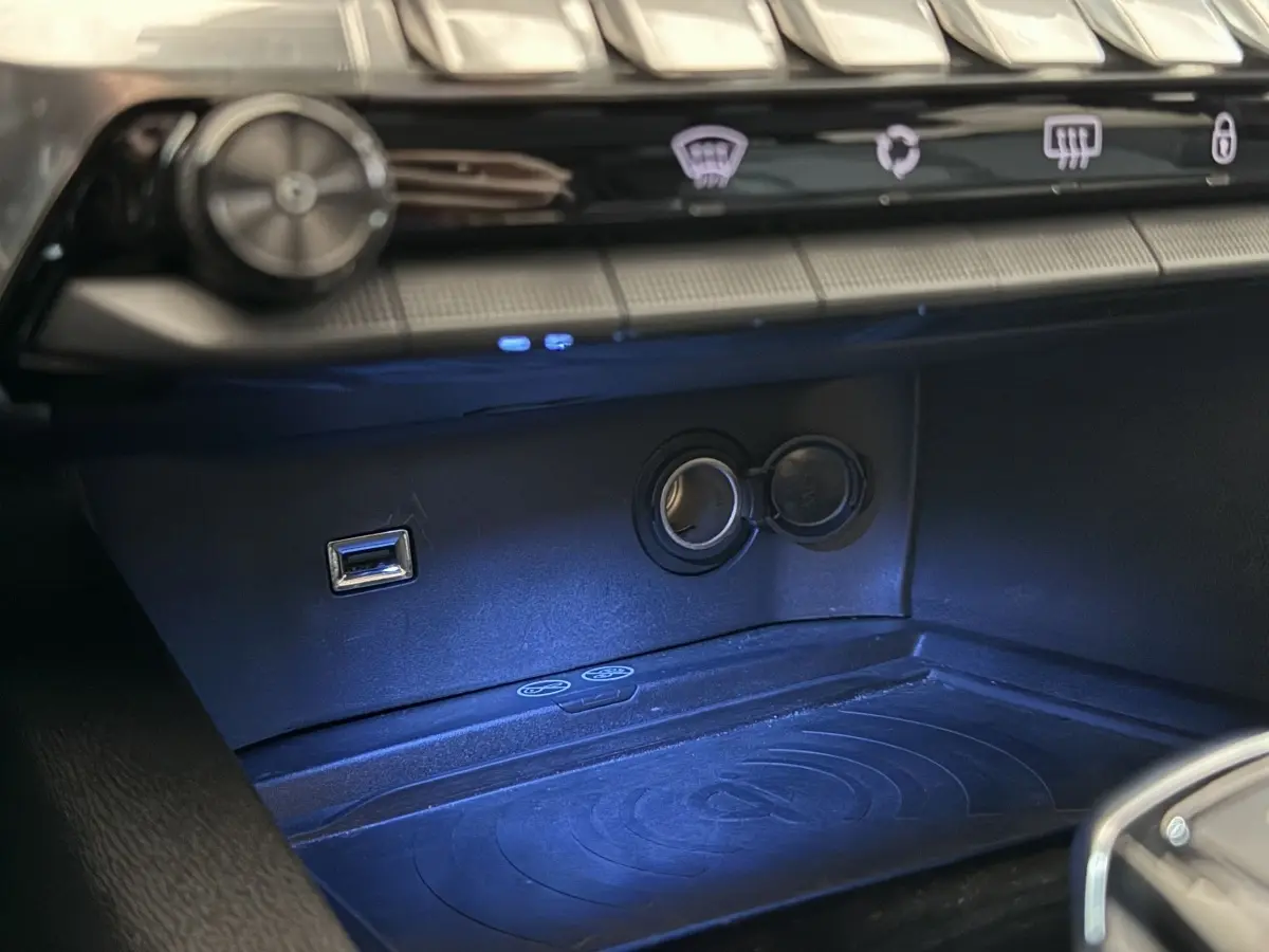 Gros plan sur la prise USB et l’allume-cigare dans l’espace de rangement avant du Peugeot 5008 gris clair 2021.