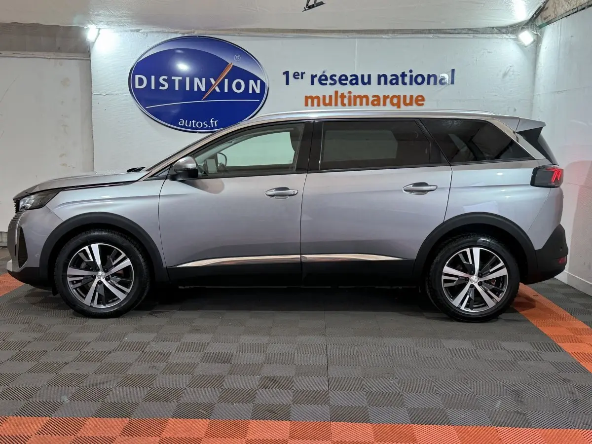 Vue de profil côté gauche d’un Peugeot 5008 gris clair avec jantes alliage et vitres teintées en intérieur showroom.