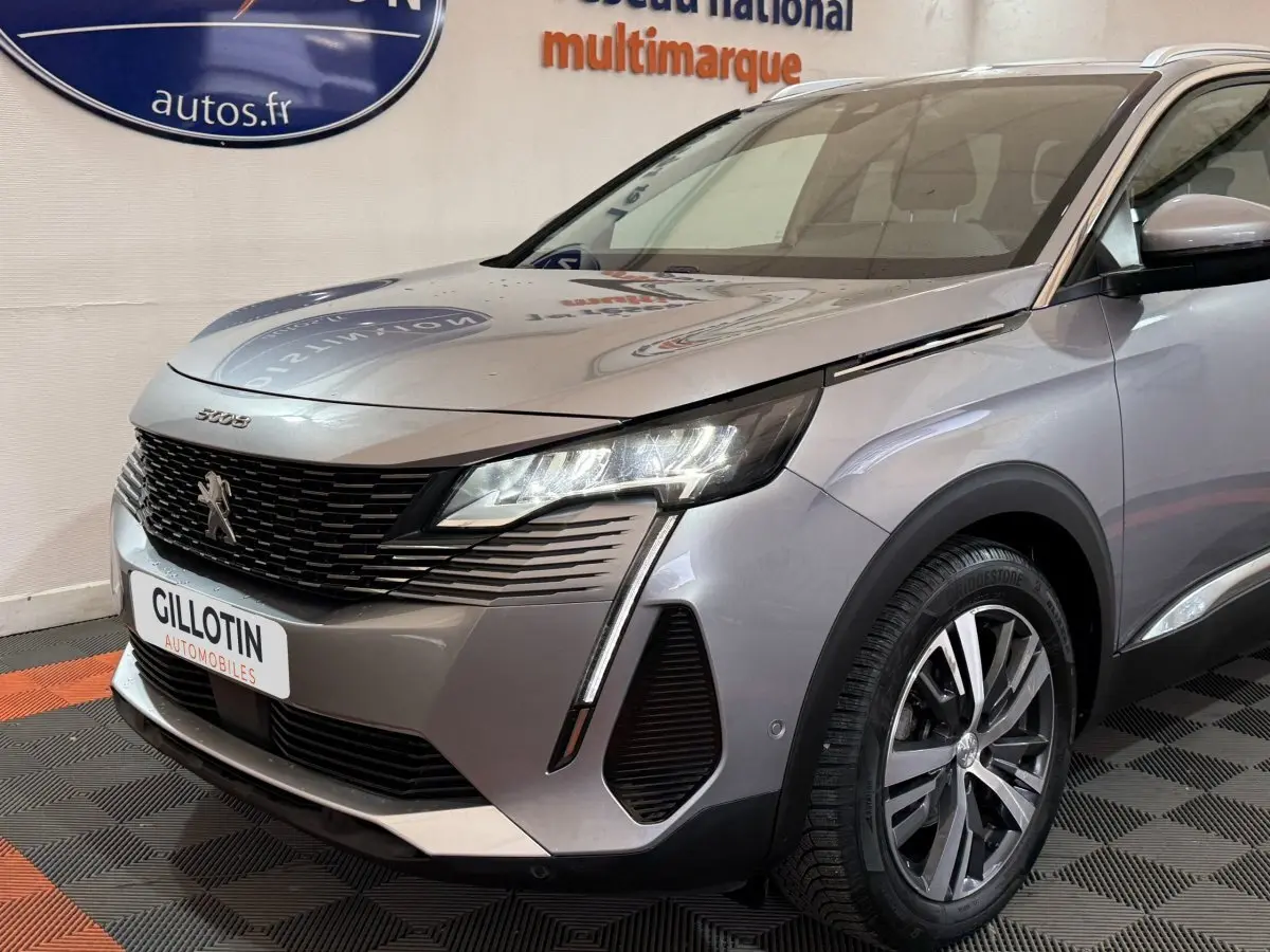 Vue 3/4 avant droit du Peugeot 5008 gris clair 2021 avec phares LED et calandre noire distinctive.