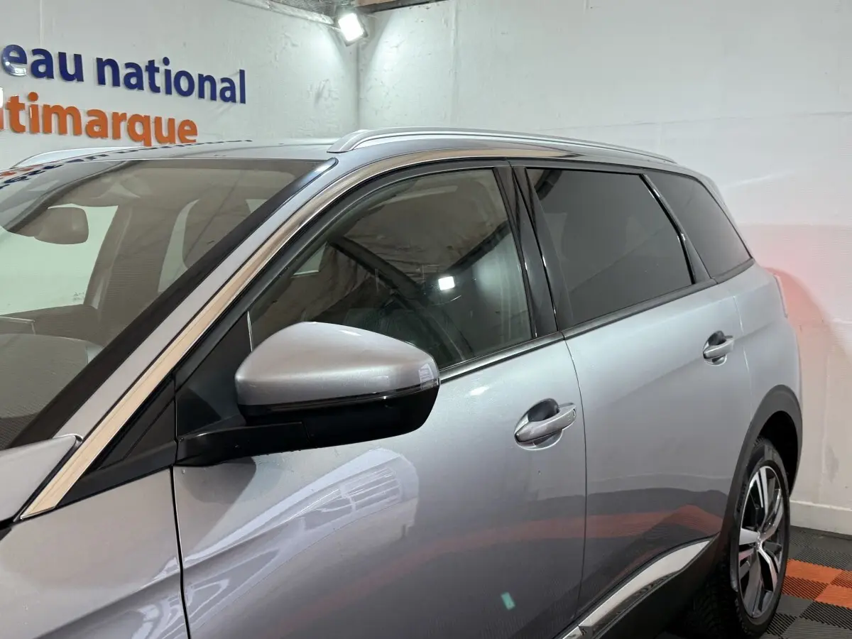 Vue latérale droite d'un Peugeot 5008 gris clair avec rétroviseurs électriques et vitres teintées dans un showroom.
