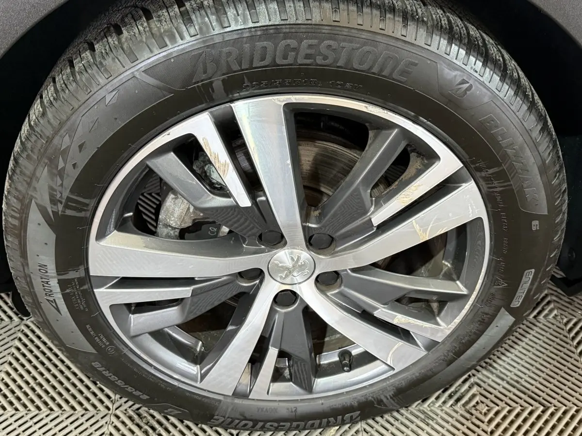 Gros plan sur la roue avant droite du Peugeot 5008 gris clair, jante alliage à design moderne avec logo lion central.