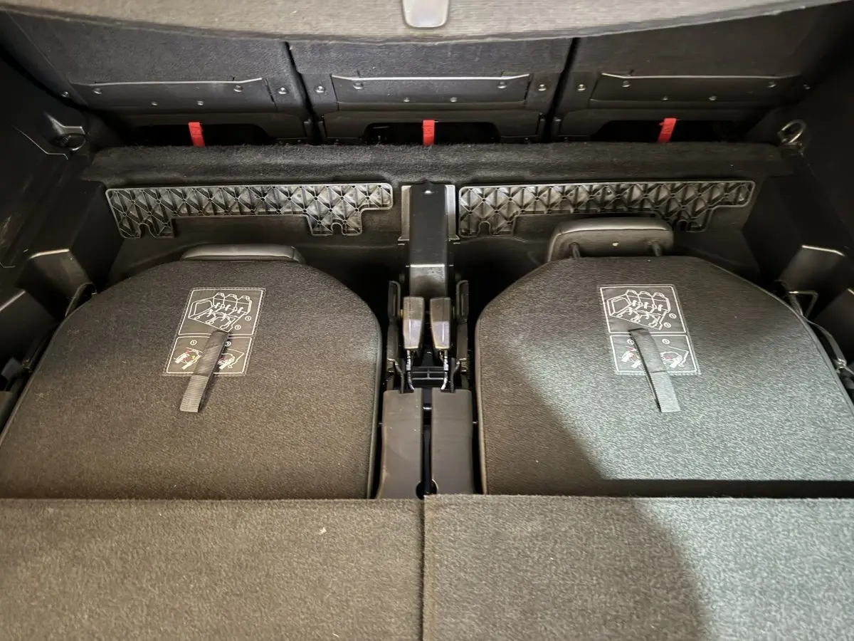 Vue plongeante sur le coffre du Peugeot 5008 gris clair avec sièges arrière rabattus et sangles de déploiement visibles.