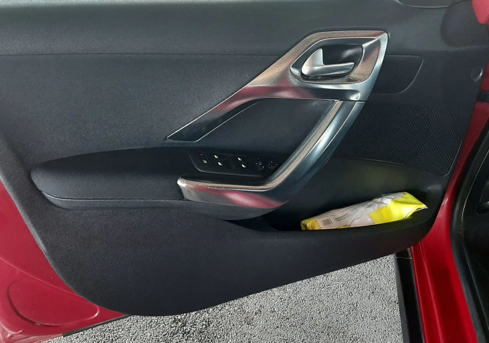 Porte côté gauche ouverte d'un Peugeot 2008 rouge, avec commandes de vitres et poignée argentée visible.