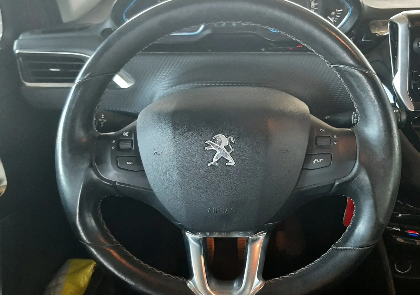 Vue rapprochée du volant en cuir noir du Peugeot 2008 2016, avec commandes intégrées et tableau de bord en arrière-plan.