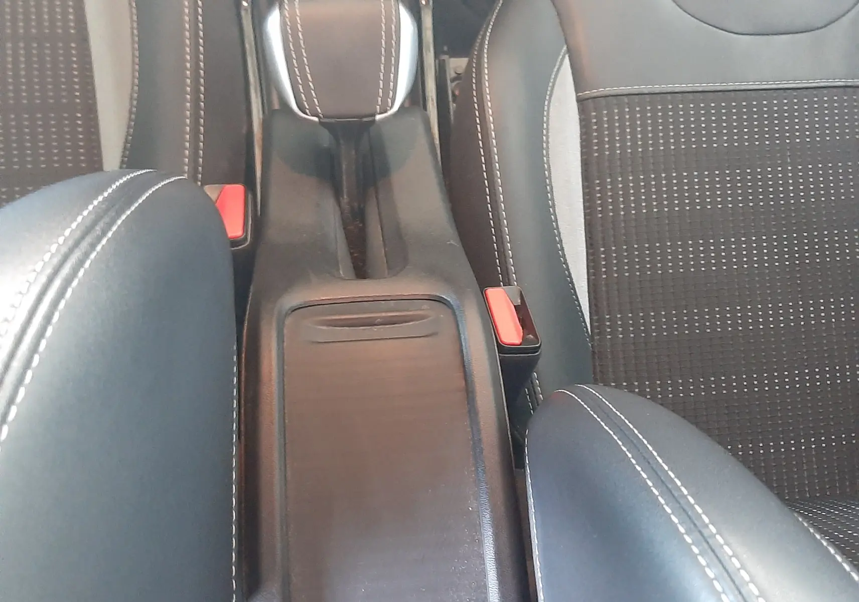 Vue plongeante sur la console centrale noire et les sièges en tissu noir avec surpiqûres blanches du Peugeot 2008 rouge 2016.