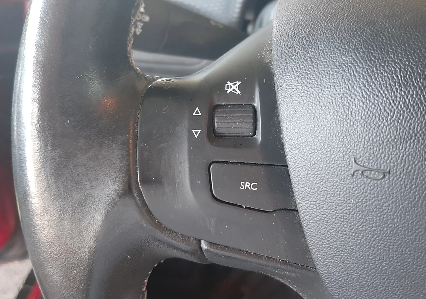 Gros plan sur les commandes audio au volant noir du Peugeot 2008 rouge 2016, bouton SRC et molette de volume.