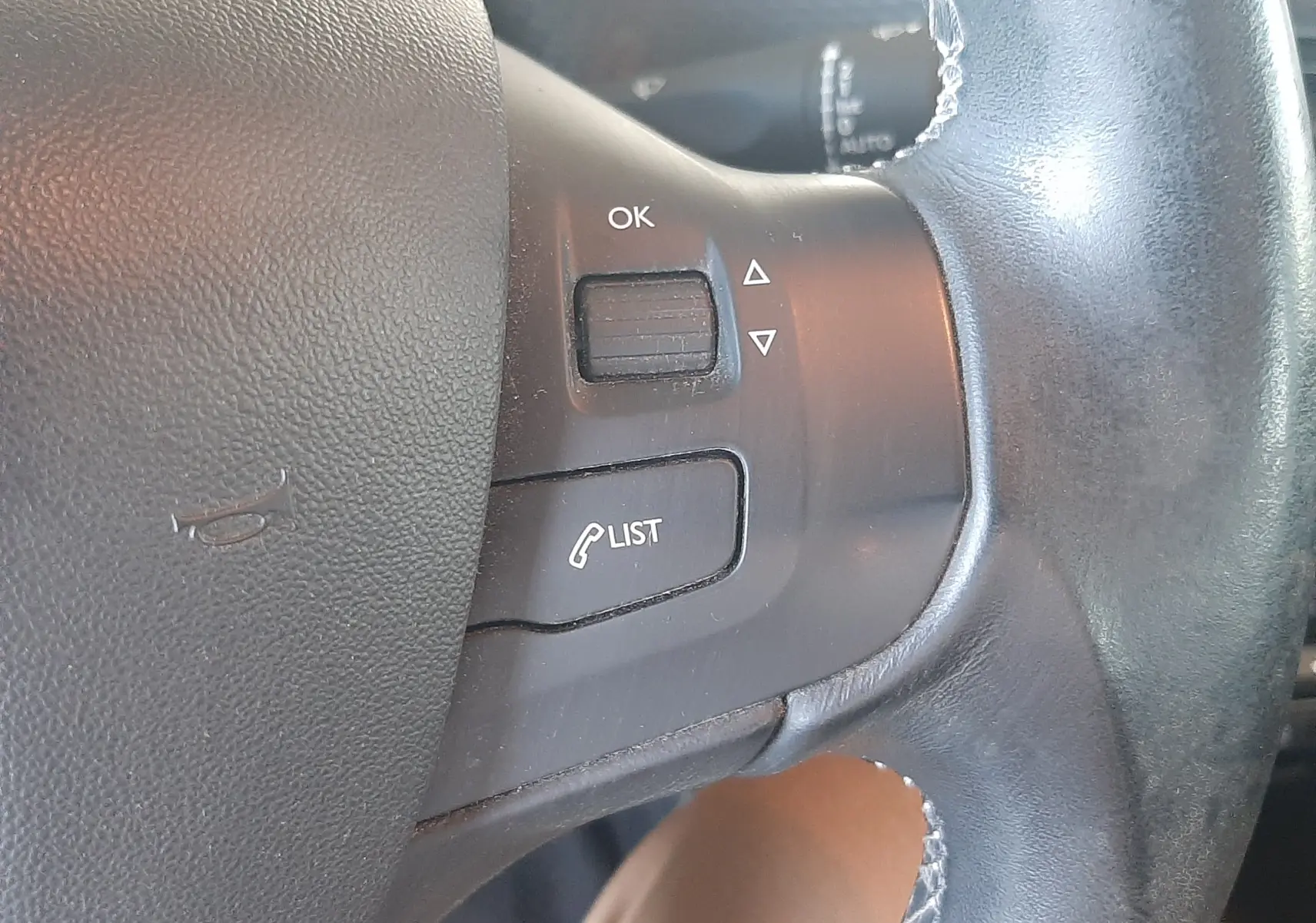 Gros plan sur les commandes à droite du volant noir d'une Peugeot 2008 rouge, boutons OK et LIST visibles.