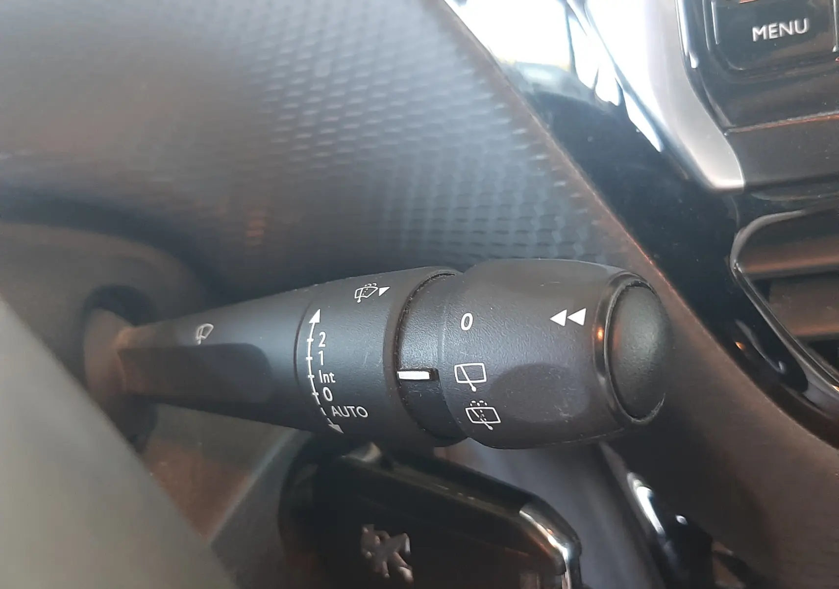 Gros plan sur la commande des essuie-glaces à gauche du volant dans l'habitacle noir du Peugeot 2008 rouge 2016.