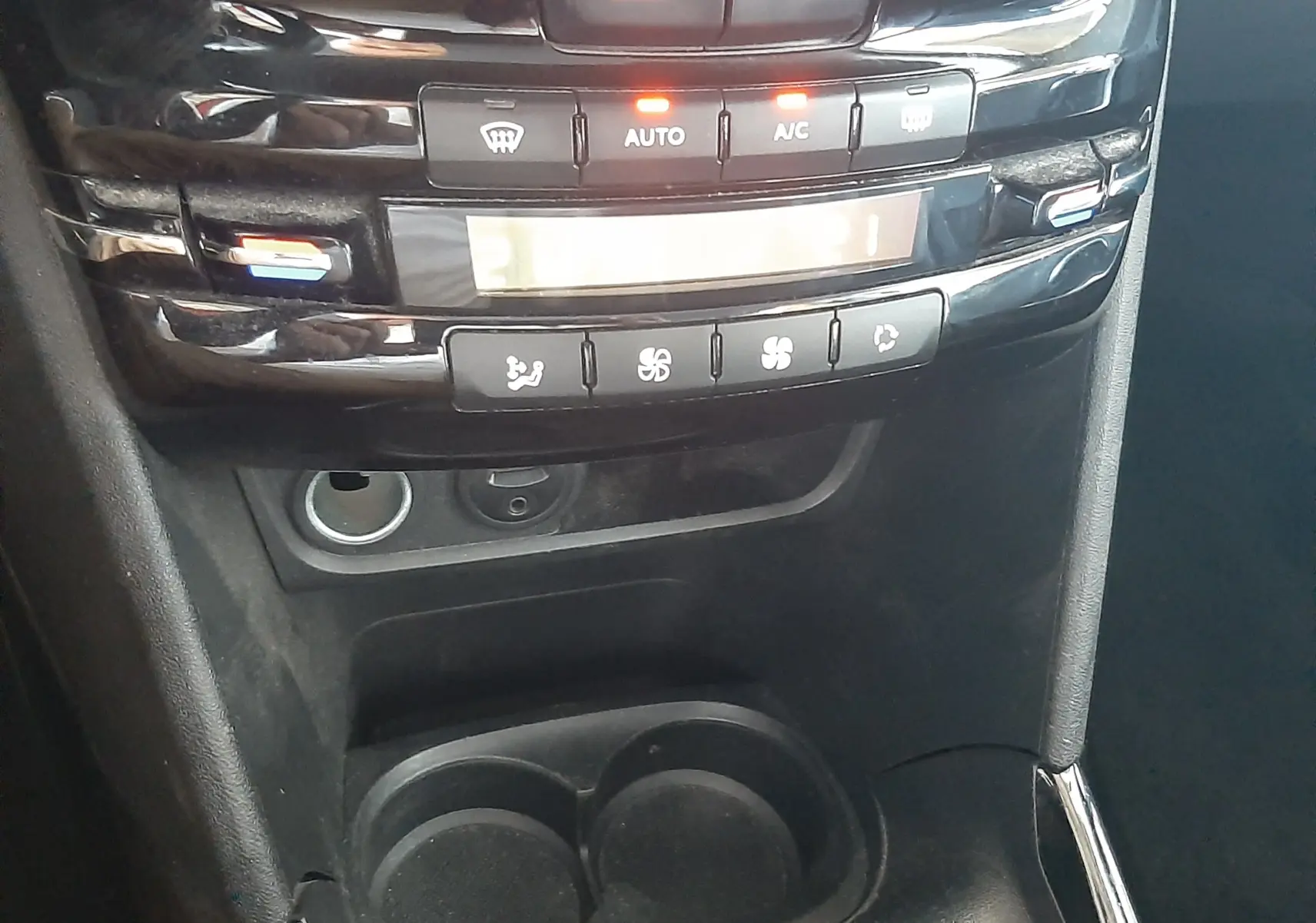 Vue rapprochée de la console centrale noire de la Peugeot 2008 rouge, montrant les commandes de climatisation et porte-gobelets.