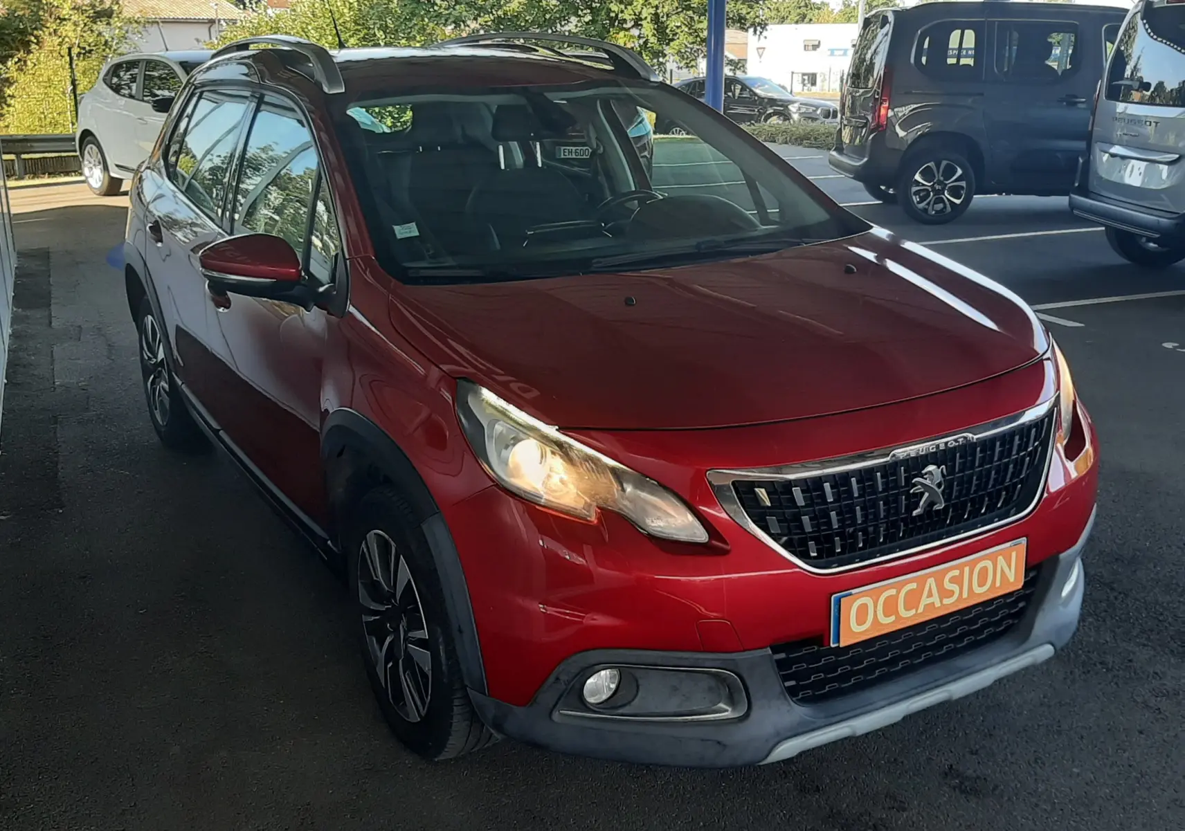 Peugeot 2008 rouge vue 3/4 avant droit avec phares allumés et plaque "OCCASION" en concession.