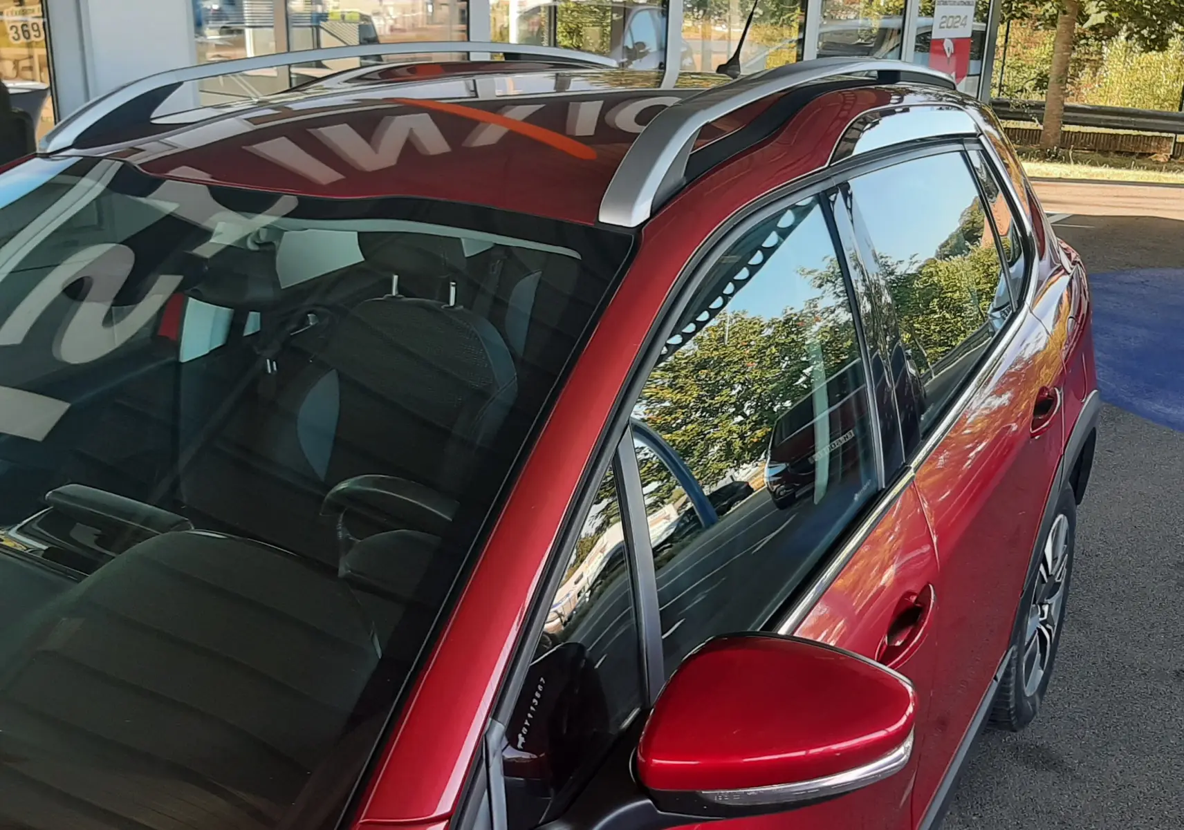 Vue de côté droit avant du Peugeot 2008 rouge avec barres de toit argentées et rétroviseur assorti.