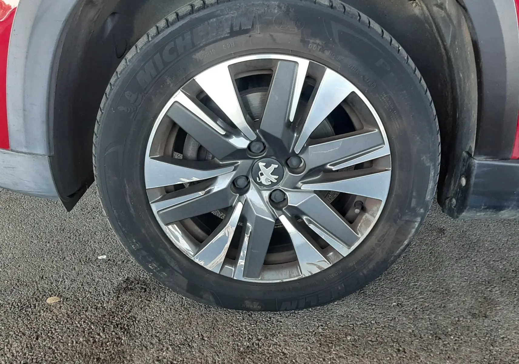 Gros plan sur la roue avant gauche d'une Peugeot 2008 rouge, jante alliage à motif moderne et pneu Michelin visible.