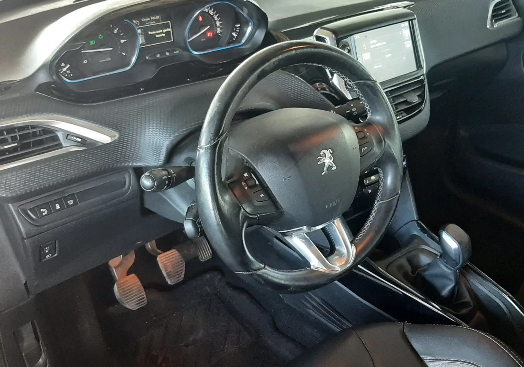 Vue intérieure côté conducteur du Peugeot 2008 rouge de 2016, volant multifonction et tableau de bord numérique visibles.