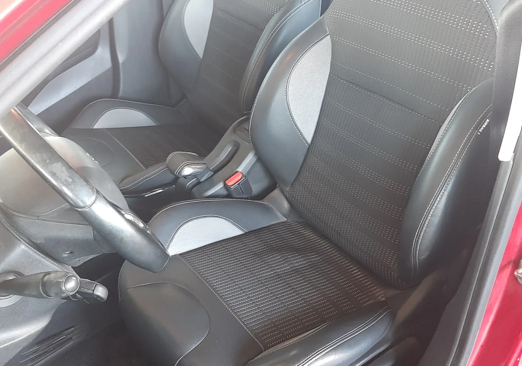 Vue intérieure côté gauche du Peugeot 2008 rouge de 2016, mettant en valeur les sièges noirs en tissu et cuir.