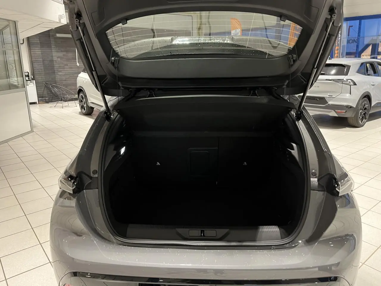 Coffre ouvert vu de l'arrière d'une Peugeot 308 gris selenium dans un showroom lumineux.