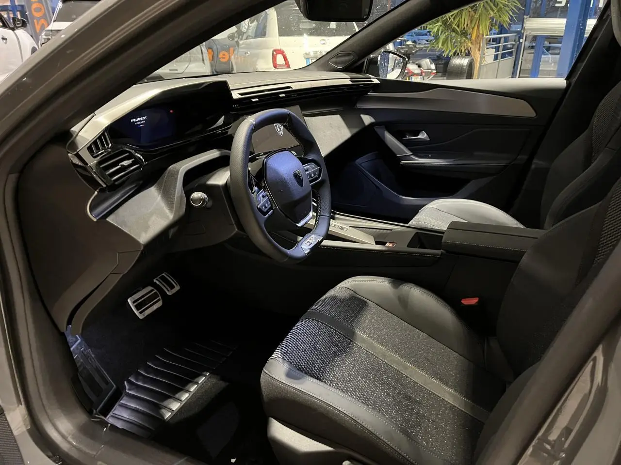 Intérieur de la Peugeot 308 GT 2024 vu côté conducteur, avec volant cuir et sellerie tissu/TEP gris.