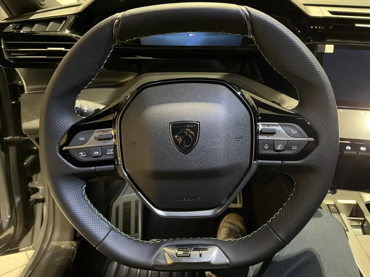 Volant cuir noir avec surpiqûres vertes et logo GT au centre d'une Peugeot 308 GT 2024, vue de face rapprochée.