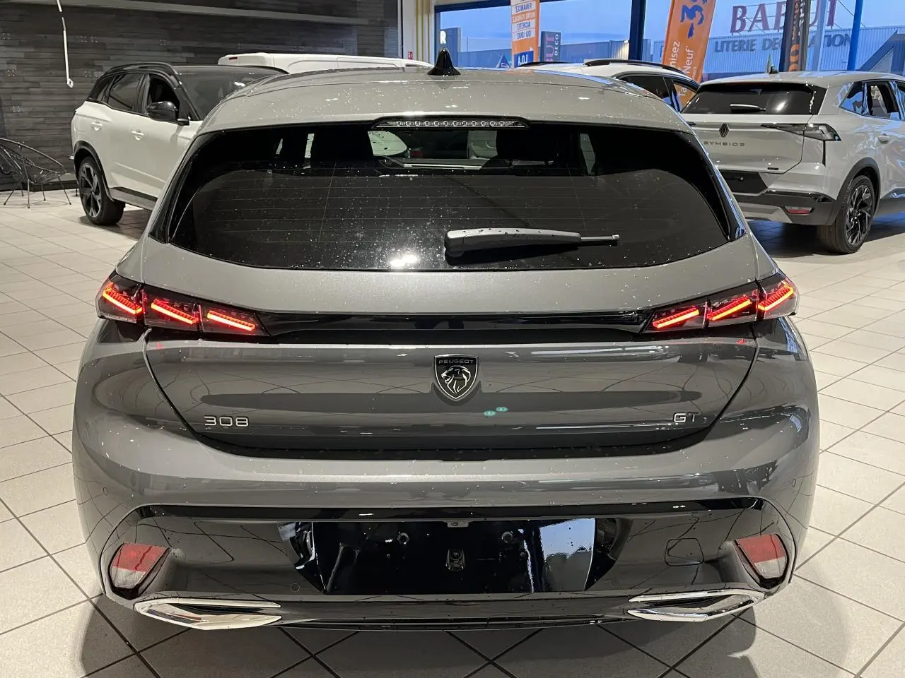 Vue arrière d'une Peugeot 308 GT gris sélénium avec feux arrière LED griffés et jantes alliage visibles en intérieur showroom.